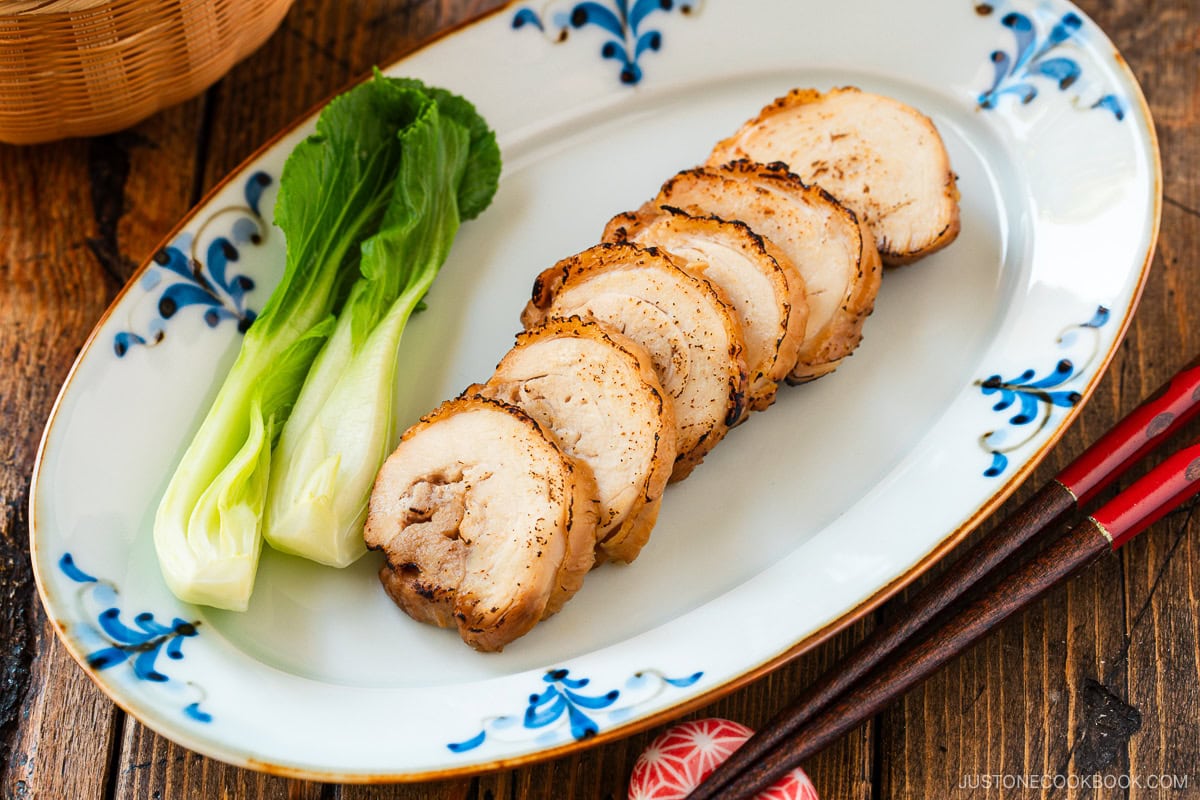 A rectangular plate containing thinly sliced, seared chicken chashu served with bok choy.