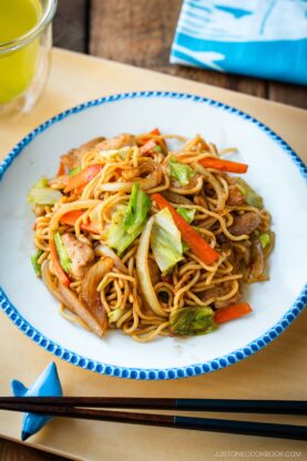 Delicious Chicken Yakisoba with tender, moist chicken thighs and crisp veggies in a sweet savory sauce plated on a beautiful white plate with blue scalloped edge.