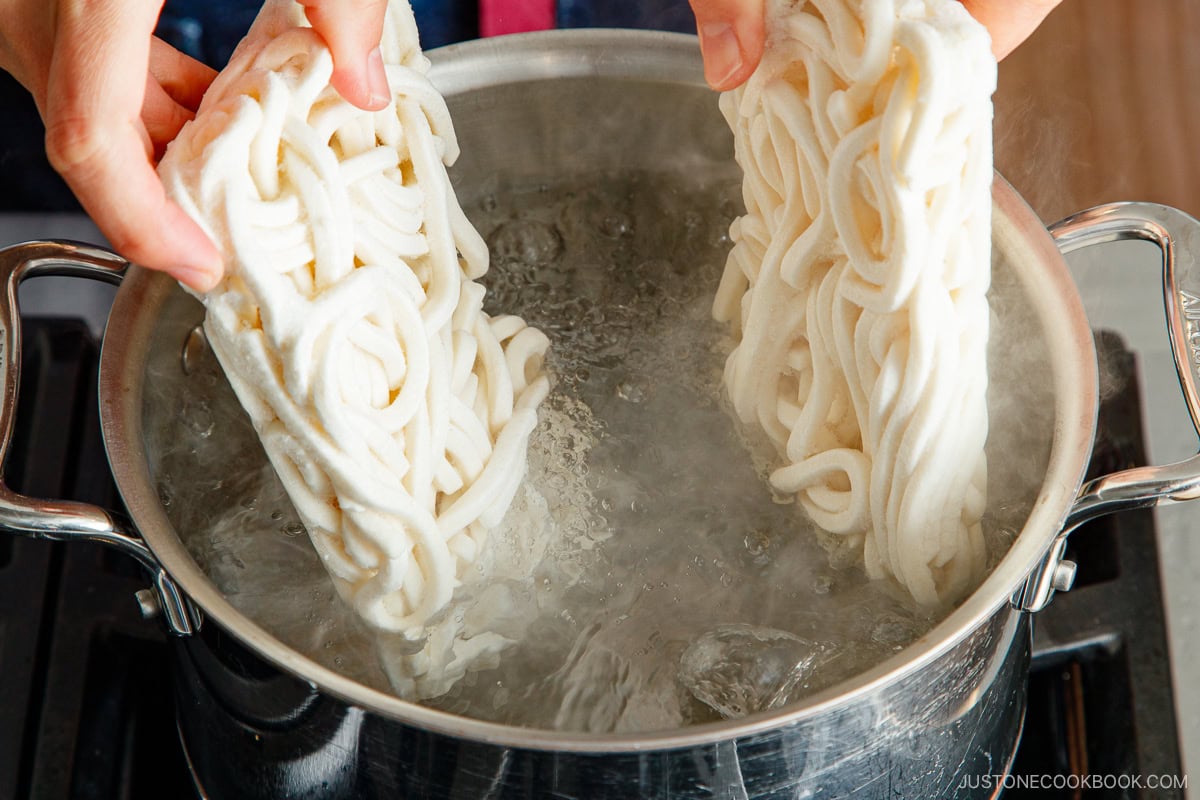 Adding frozen udon noodles to the boiling water.