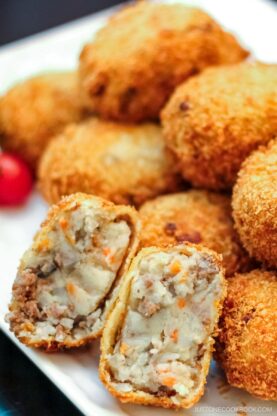 A white rectangular plate containg potato and meat croquettes.