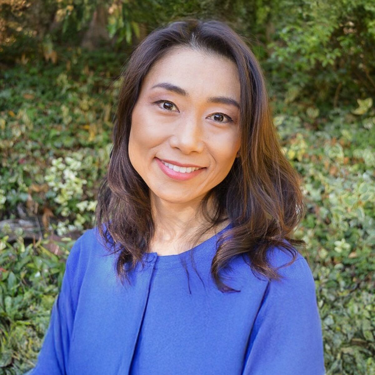 Portrait of an Asian woman smiling outdoors, wearing a bright blue top with a lush green background; perfect for highlighting cultural cuisine or lifestyle content on Just One Cookbook.