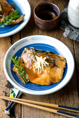 A blue Japanese plate containing Saba Misoni (Mackerel Simmered in Miso) garnished with julienned ginger.